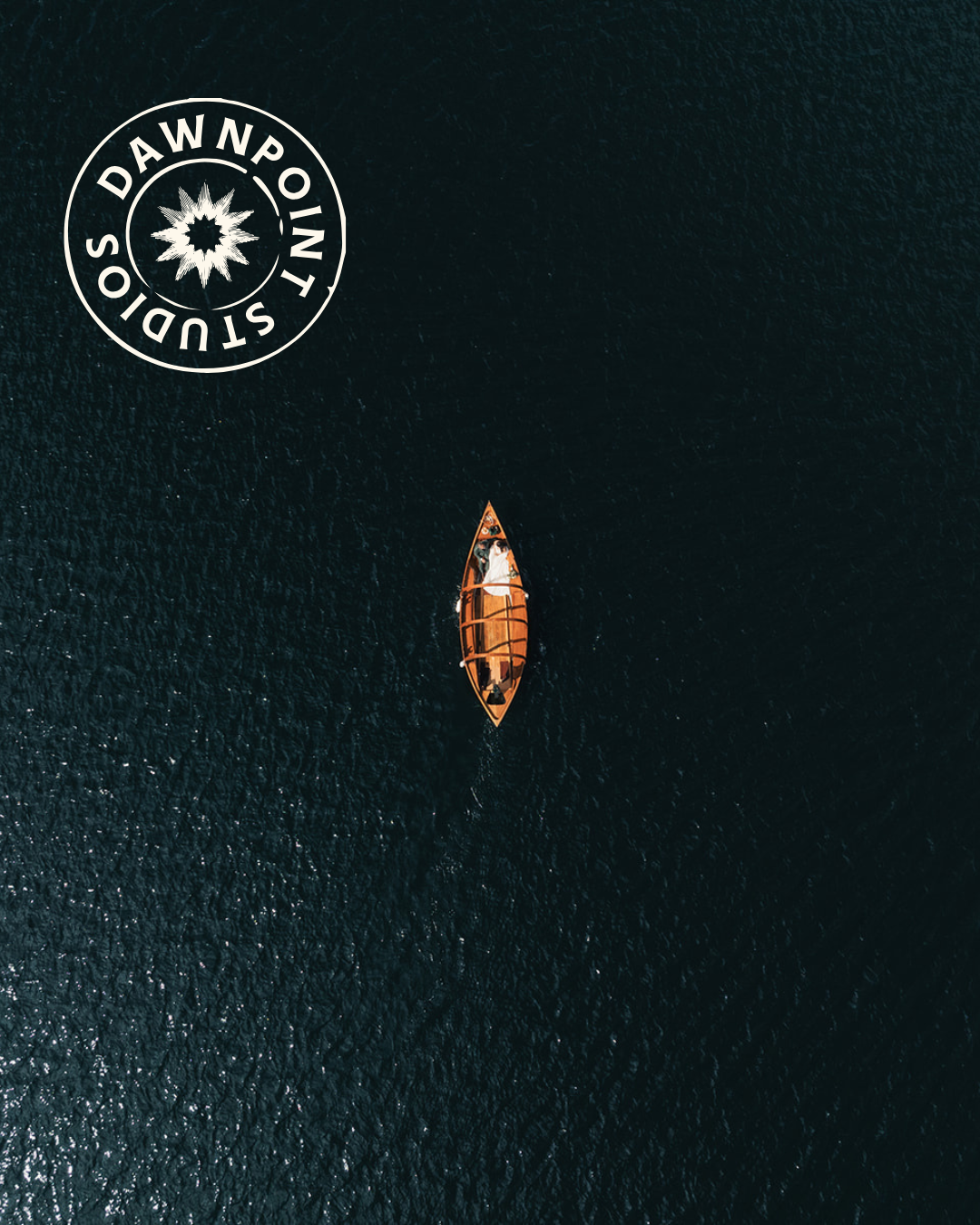 A brown canoe with a person inside floats on dark, calm water, viewed from above. A circular "Dawnpoint Studios" logo is in the top left corner.
