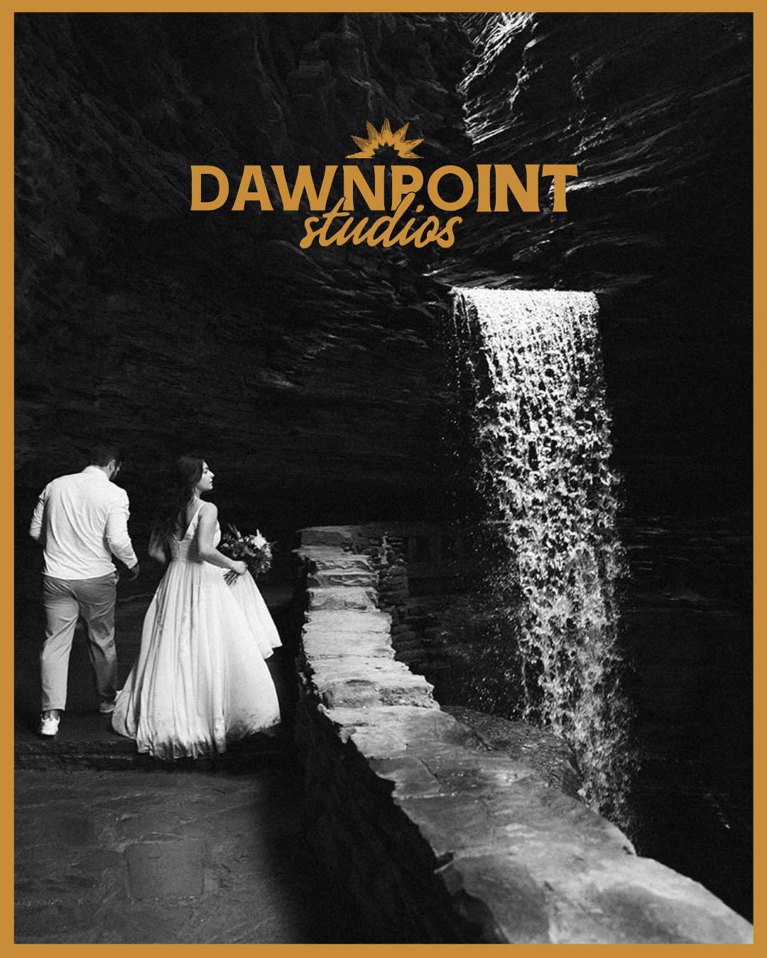 A bride and groom walk along a stone path beside a waterfall in a black and white photo with "DAWNPOINT studios" logo at the top.